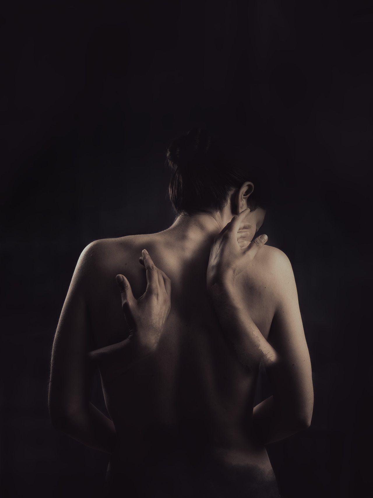 Two intertwined self-portrait figures emerging from darkness